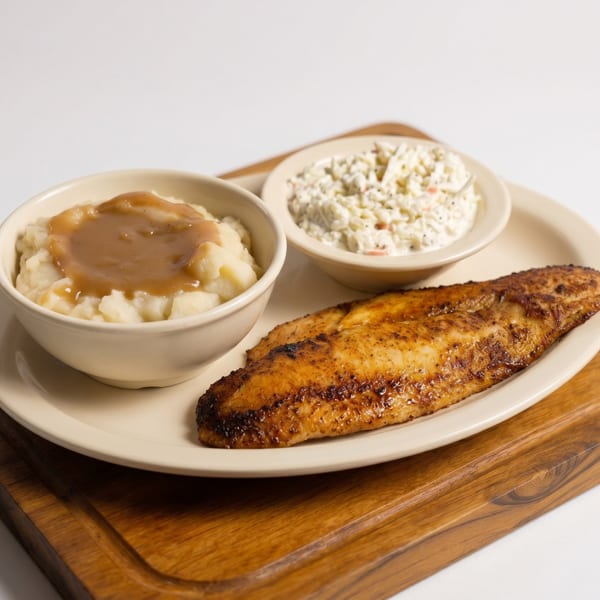 A plate of grilled fish, mashed potatoes with gravy, and coleslaw on a wooden board.