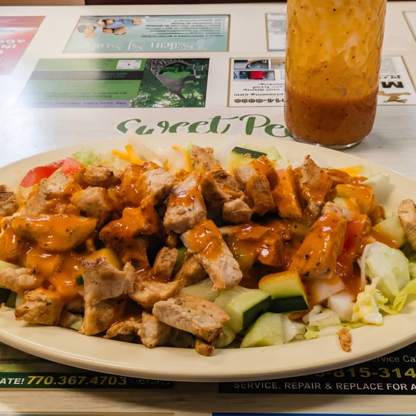 A Sweet Pea's chicken salad with orange dressing, lettuce, cucumbers, and tomatoes on a white plate.