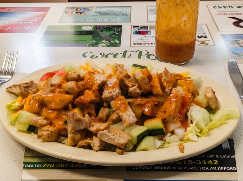 A Sweet Pea's chicken salad with orange dressing, lettuce, cucumbers, and tomatoes on a white plate.
