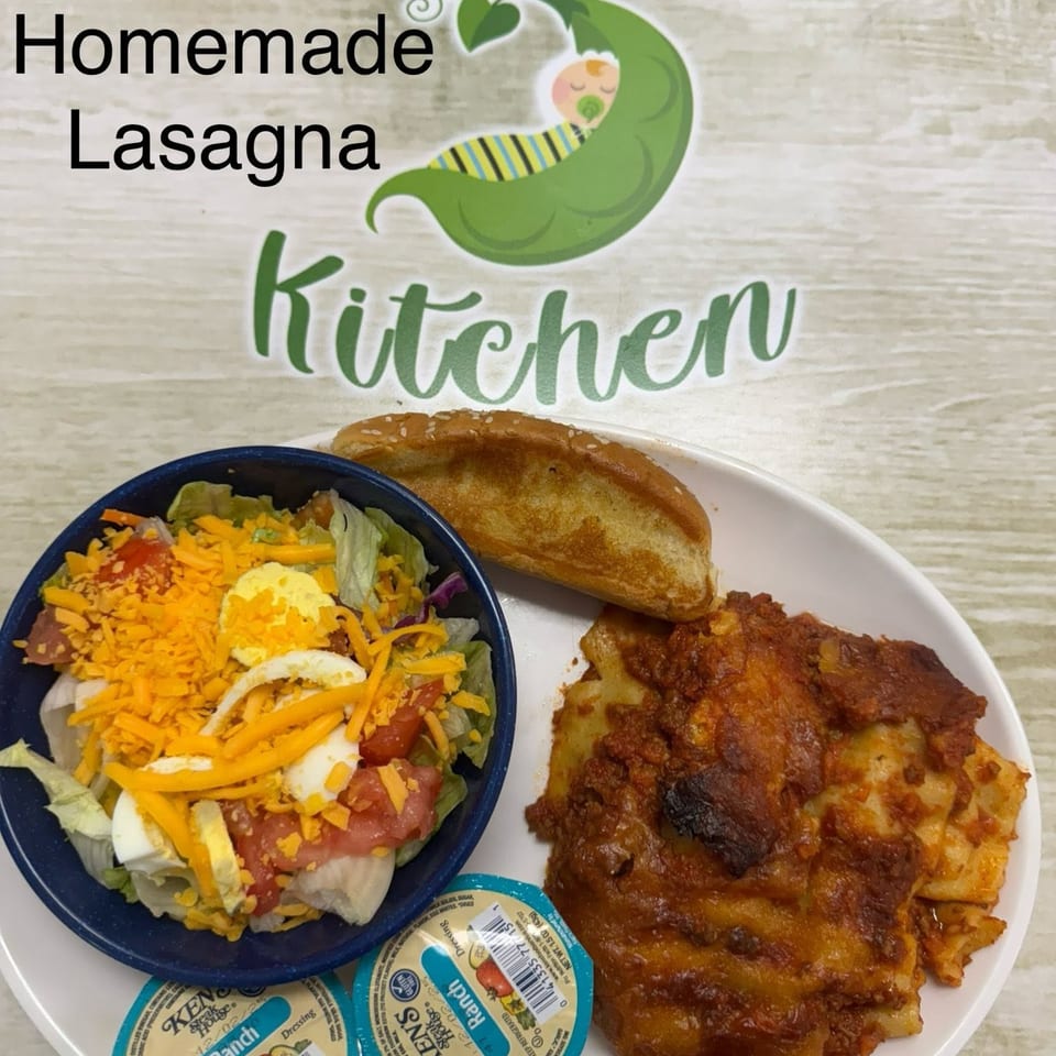 Homemade lasagna, a side salad with ranch dressing, and garlic bread on a white plate.