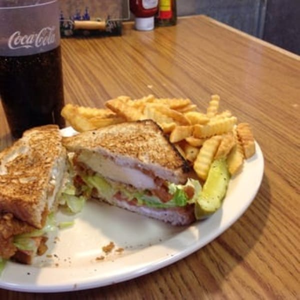 Grilled chicken sandwich with lettuce, tomato, fries, and a pickle spear on a white plate.