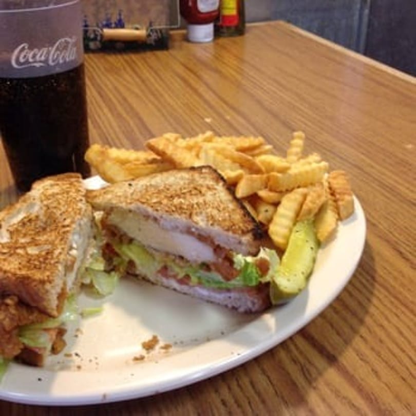 Grilled chicken sandwich with lettuce, tomato, fries, and a pickle spear on a white plate.