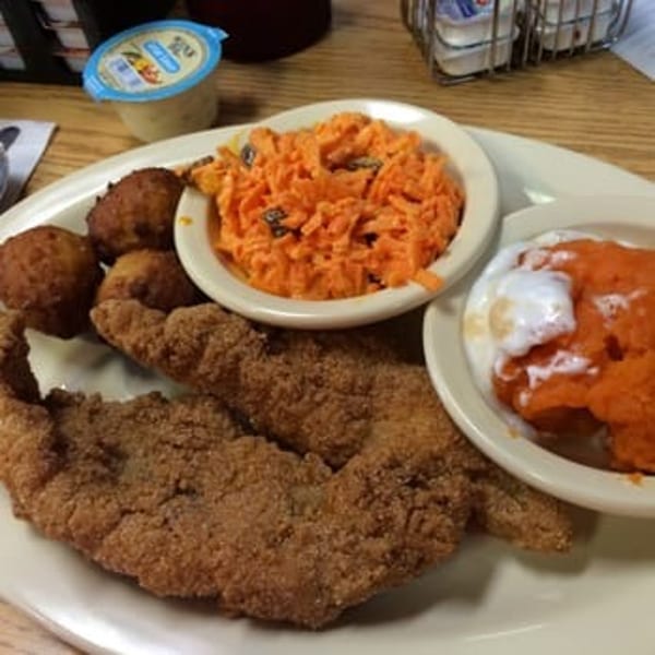 Fried fish fillets, hush puppies, carrot salad, and sweet potato casserole on a white plate.